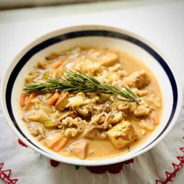 Bowl of vegan no chicken soup with tofu cubes, shredded jackfruit, vegetables, and a rosemary sprig garnish
