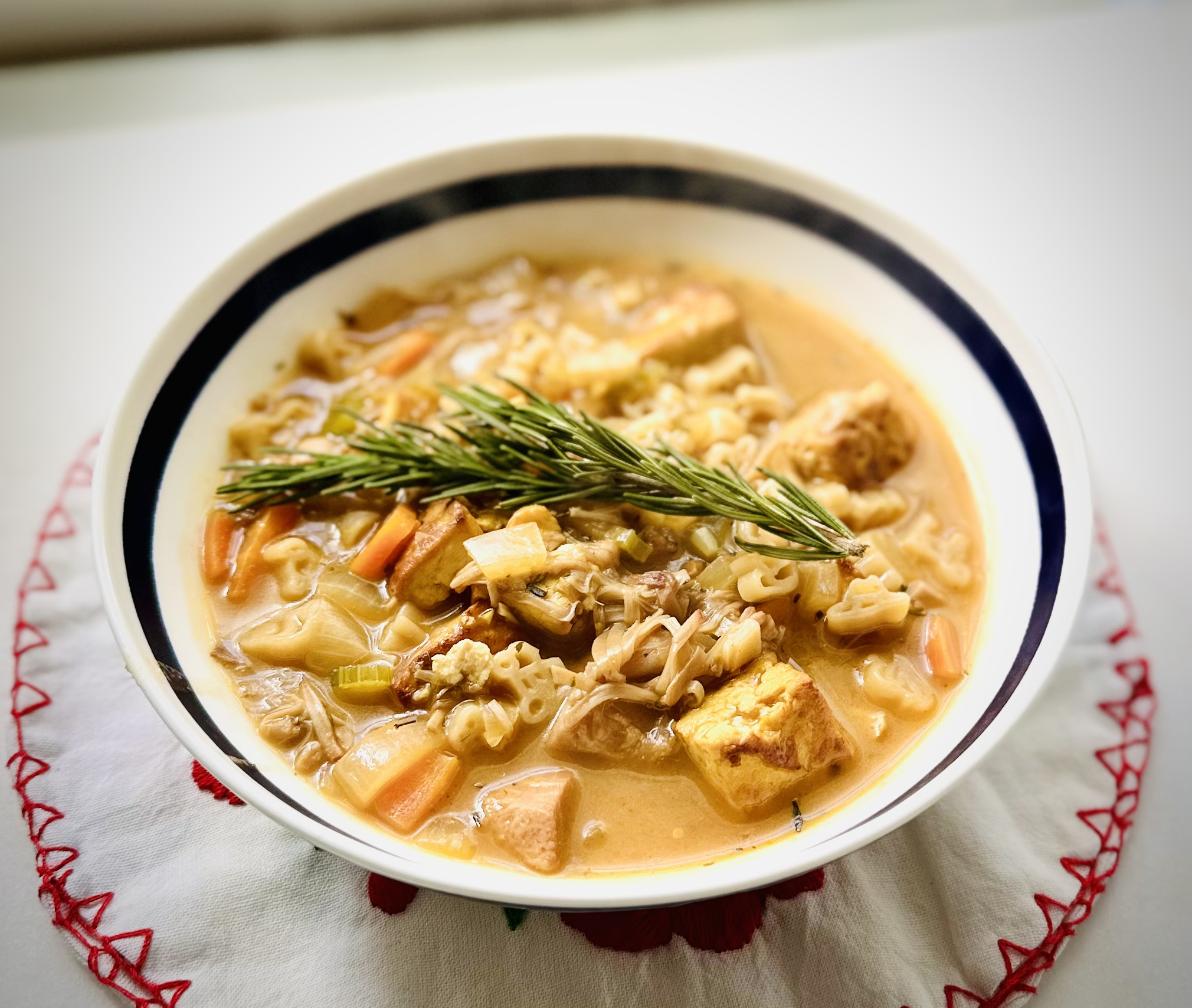 Bowl of vegan no chicken soup with tofu cubes, shredded jackfruit, vegetables, and a rosemary sprig garnish