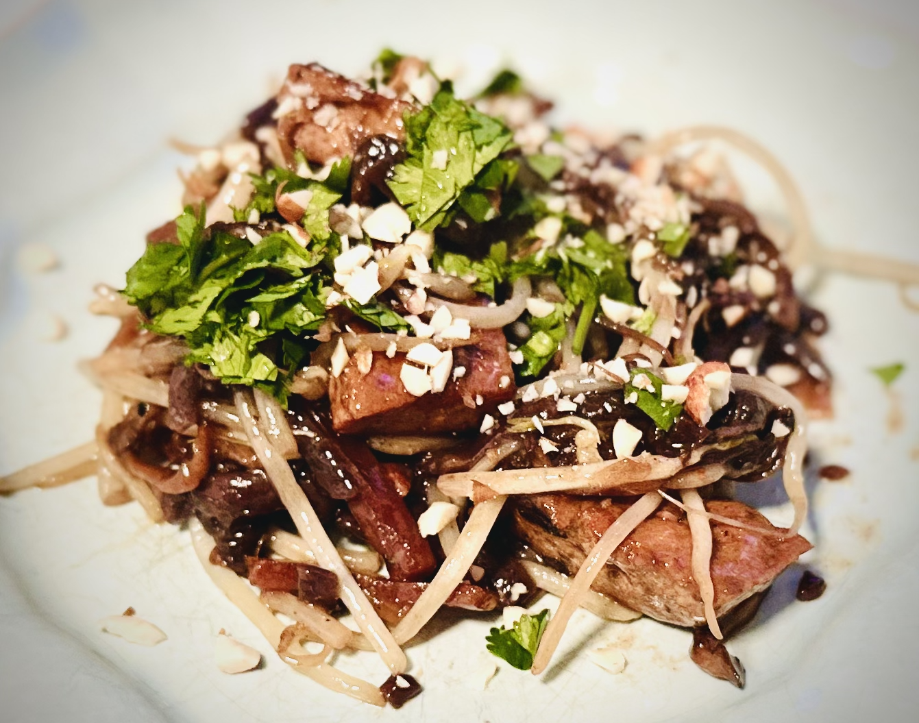 Plate of vegan pad thai with glossy rice noodles, bean sprouts, fresh cilantro, and crushed peanuts