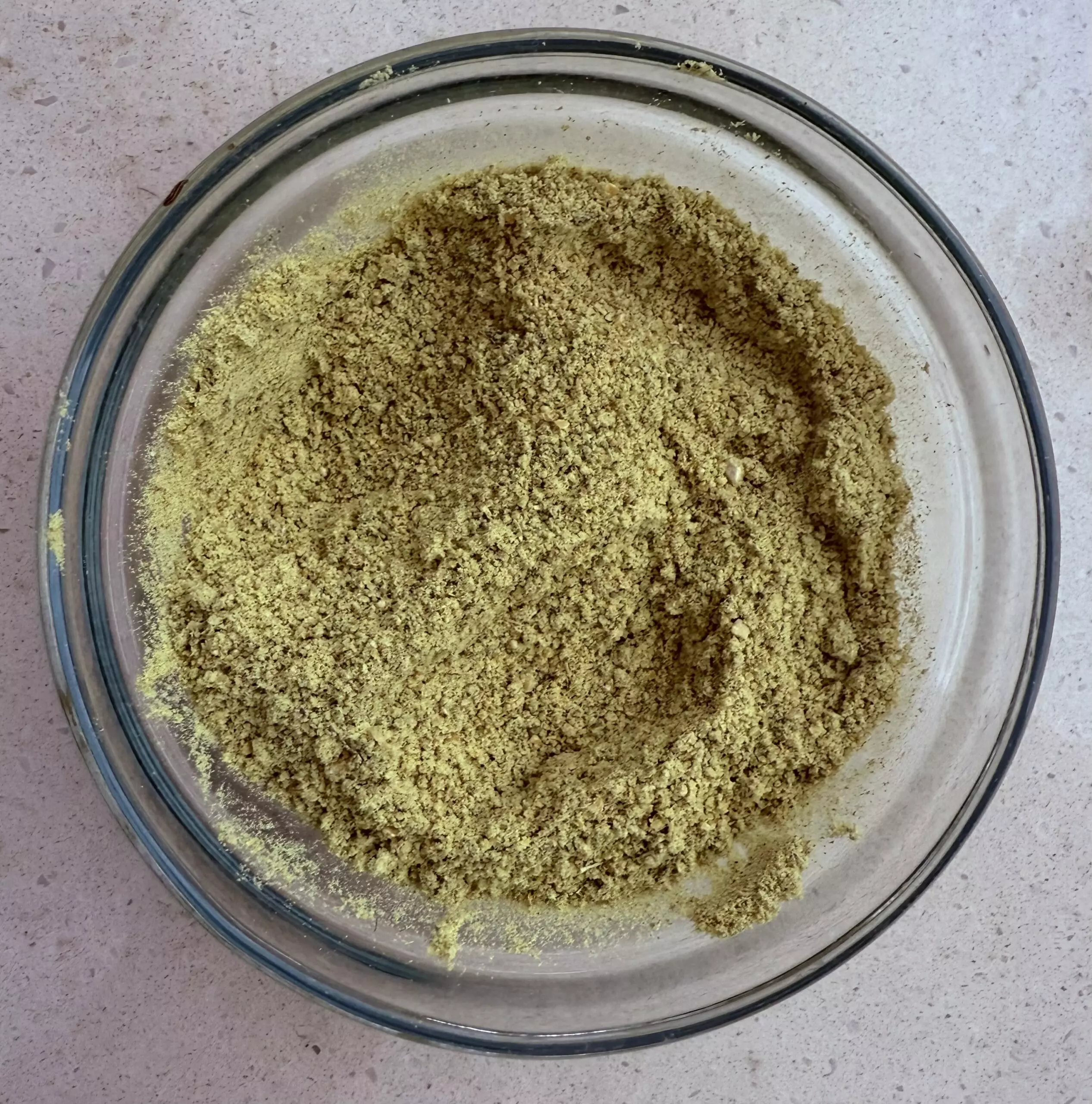 Glass bowl of freshly ground homemade sambar masala powder with a golden-green color