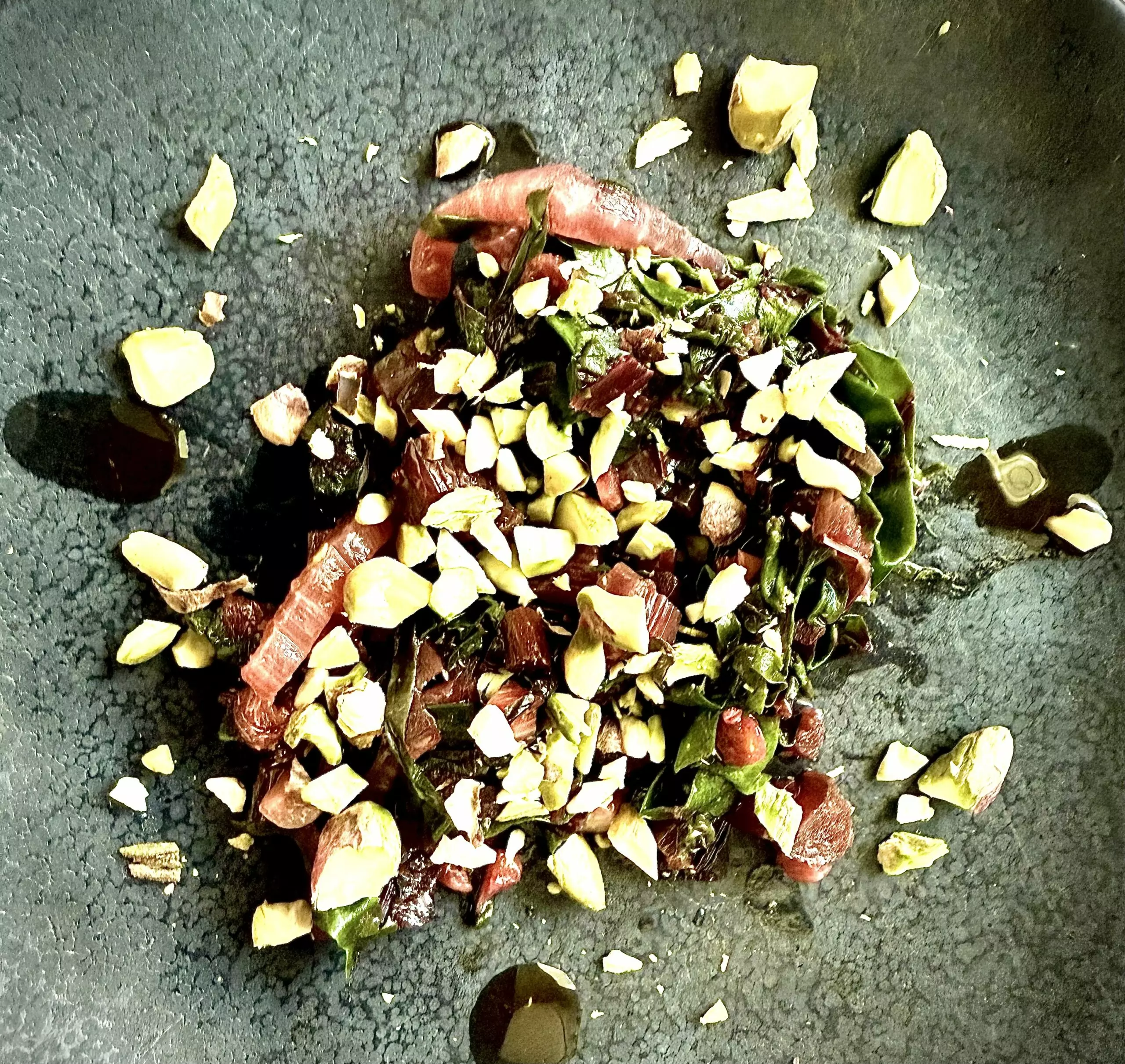 Sautéed beet greens with pink stems topped with crushed pistachios and red pepper flakes on a dark plate