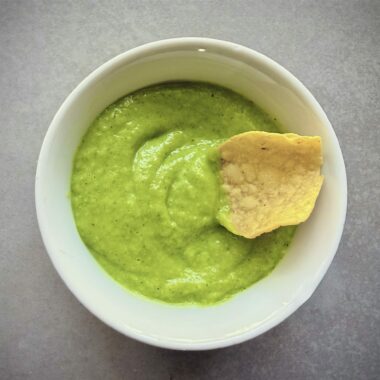 avocado-tomatillo salsa in a bowl with a chip in it