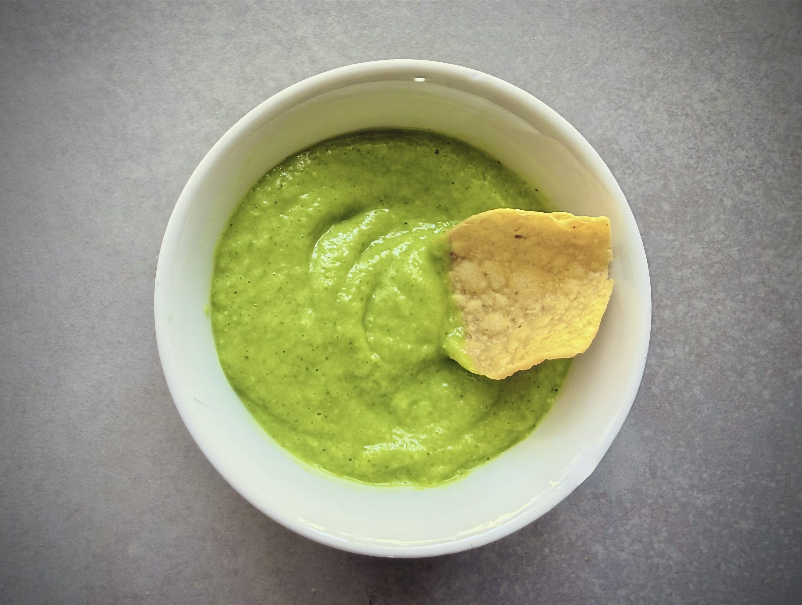 avocado-tomatillo salsa in a bowl with a chip in it