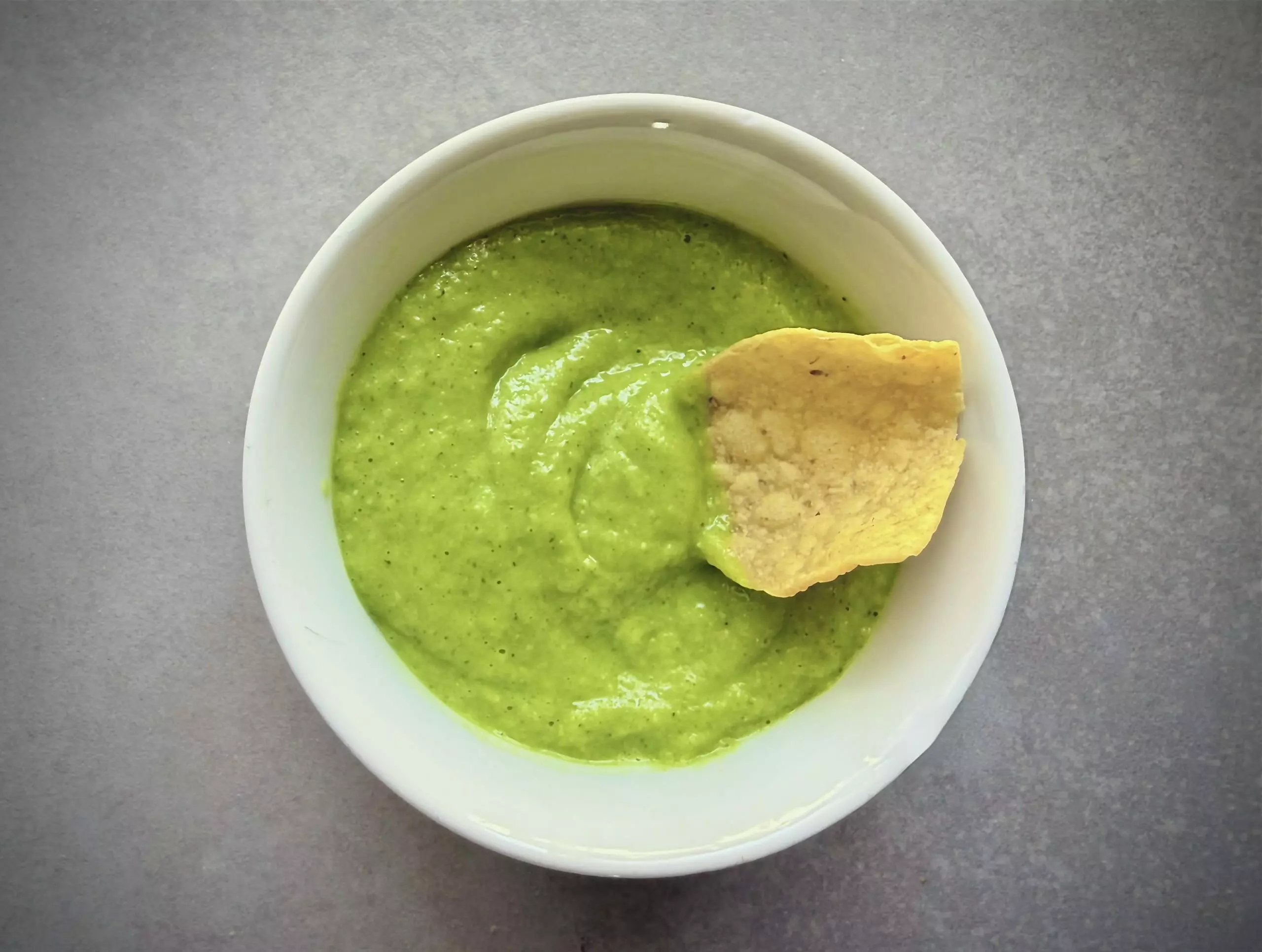 avocado-tomatillo salsa in a bowl with a chip in it