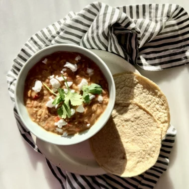 refried pinto beans in bowl topped with vegan cheese with a side of tortillas